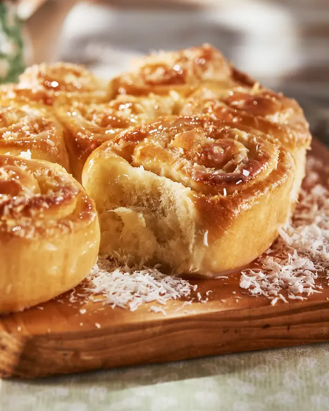 Rosca de coco em caracóis caramelizados, com miolo fofinho à mostra e coco ralado espalhado pela tábua