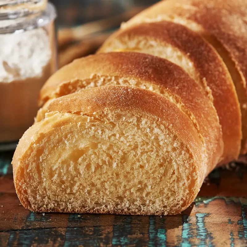 Pão caseiro fatiado com miolo macio e casca dourada, sobre madeira rústica azul-turquesa